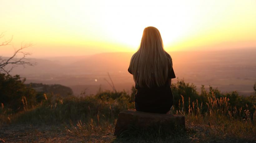 Junge Frau sitzt auf einem Felsen und schaut in den Sonnenuntergang.