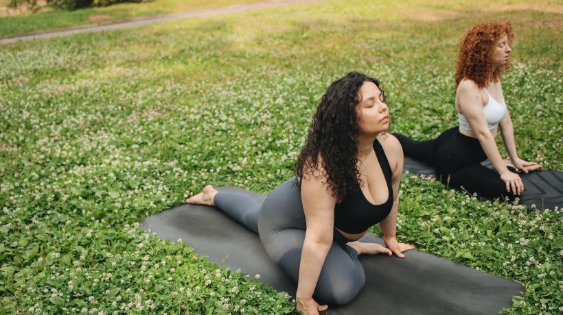 Zwei Frauen machen Yoga auf einer Wiese.