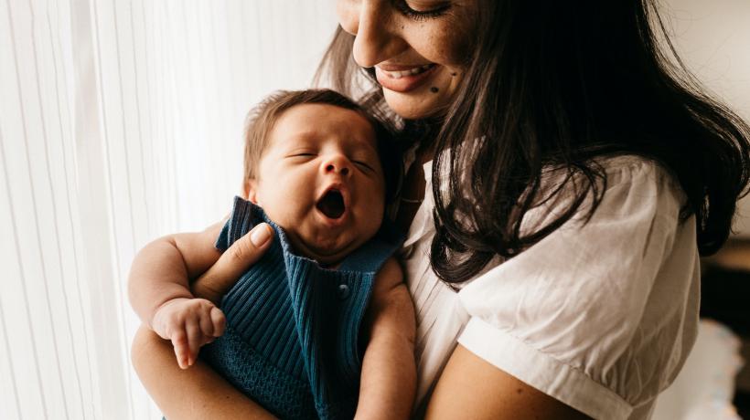 Eine Frau hält ein Baby auf dem Arm, das herzhaft gähnt.