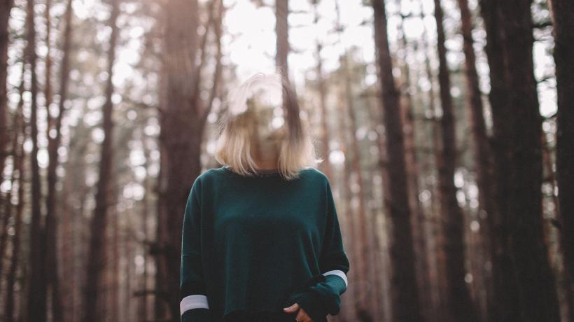 Eine Frau steht im Wald, ihr Kopf ist teilweise transparent als würde sie verblassen oder sich in Luft auflösen.