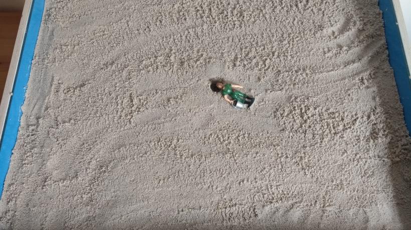 Eine einzelne Spielfigur umgekippt im sonst leeren Sandkasten