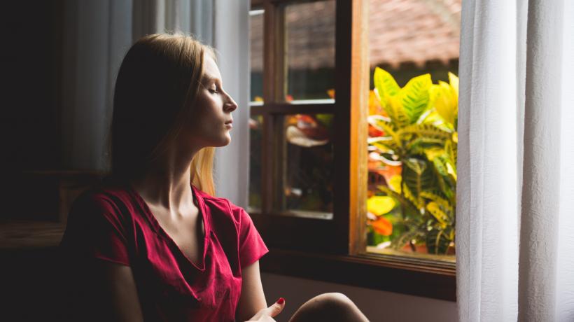 Eine Frau sitzt mit geschlossenen Augen am offenen Fenster.