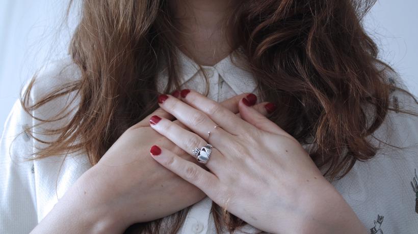 Hände einer Frau mit rotem Nagellack liegen übereinander auf ihrer Brust.