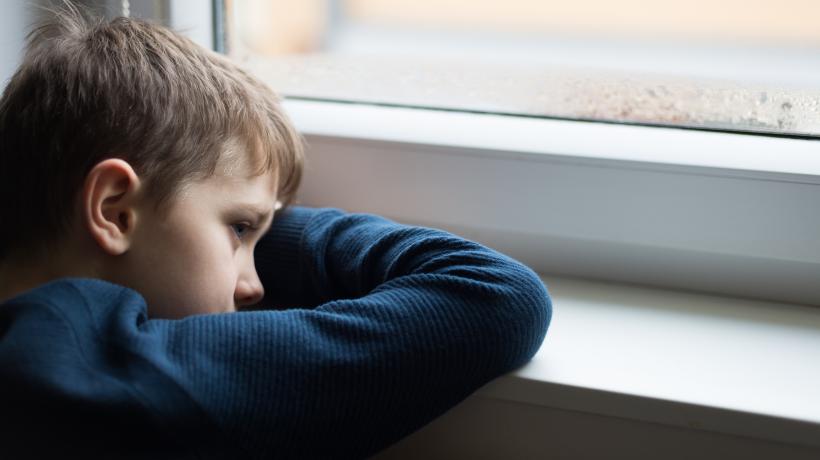 (Foto: AdobeStock) Ein kleiner Junge schaut traurig aus dem Fenster.