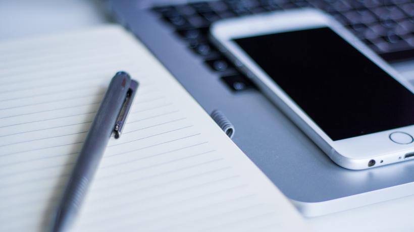 Arbeitsplatz mit Laptop, Smartphone, Stift und Notizblock