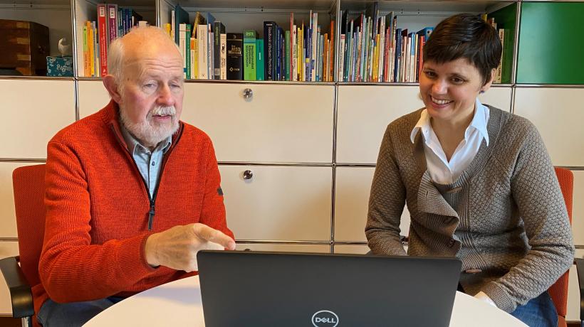 Ein älterer Mann und eine Psychologin schauen auf einen Laptop.
