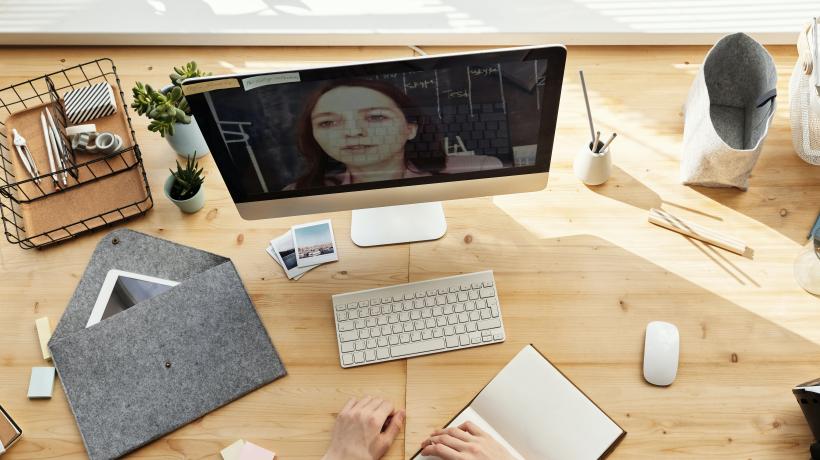 Schreibtisch mit Bildschirm auf dem eine Frau in einem Videochat zu sehen ist.