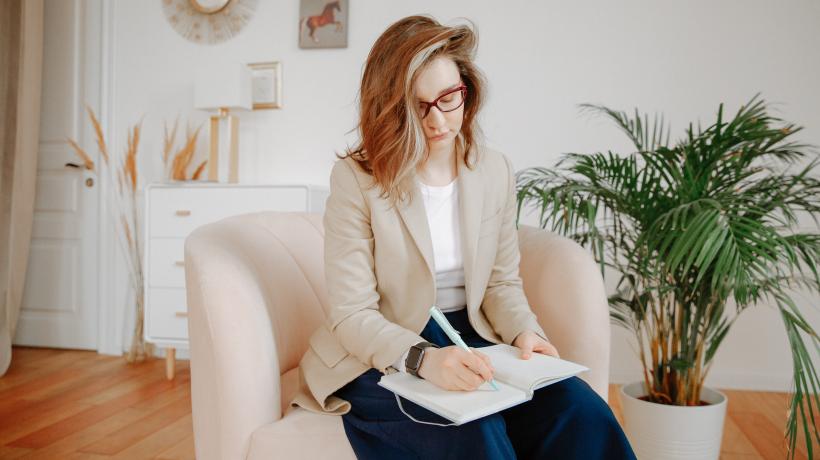 (Foto: Polina Zimmermann – Pexels.com) Blonde Frau sitzt auf einem Sessel und schreibt in ein Buch.