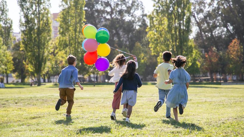Kinder laufen mit Luftballons über eine Wiese
