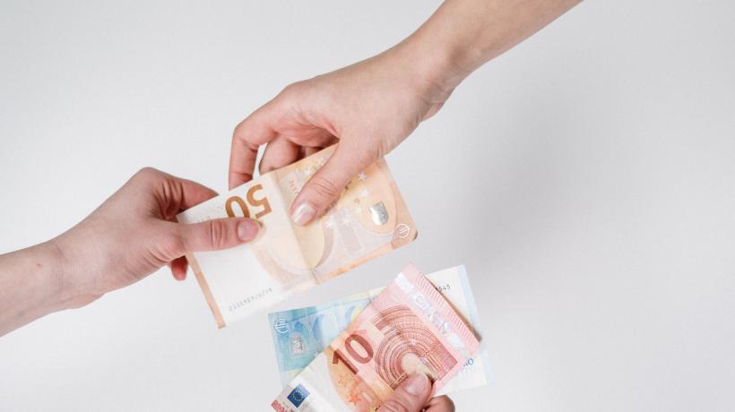 Eine Hand reicht einer anderen einen 50-Euro-Schein. Eine dritte Hand hält einen 10- und einen 20-Euro-Schein.