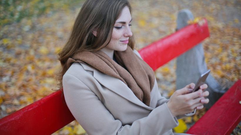 Frau sitzt mit Smartphone in der Hand auf einer Parkbank.