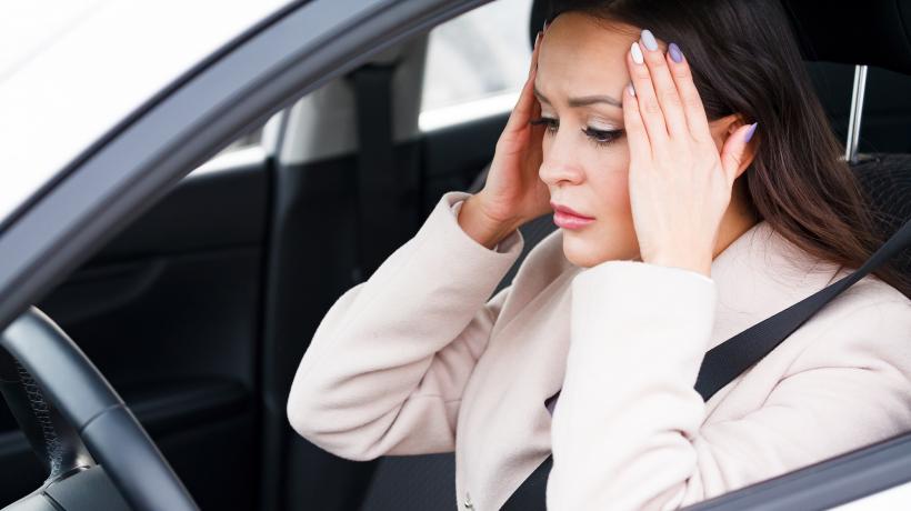 Foto: Nobilior – AdobeStock Frau sitzt am Steuer und hält sich ängstlich mit beiden Händen die Schläfen.