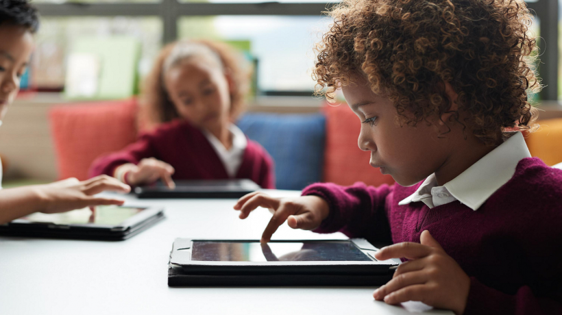 Foto: Getty Images Drei Kinder sitzen am Tisch und tippen jeweils auf einem iPad herum.