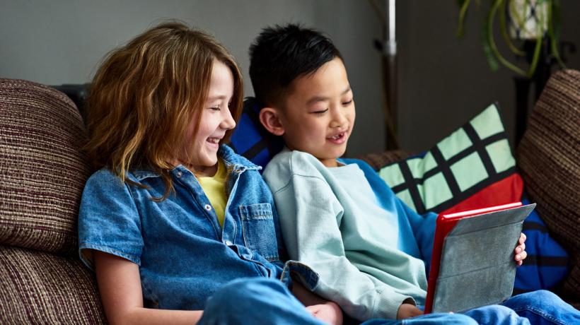 Foto: Getty Images Zwei Kinder sitzen mit einem iPas auf dem Schoß auf der Couch.
