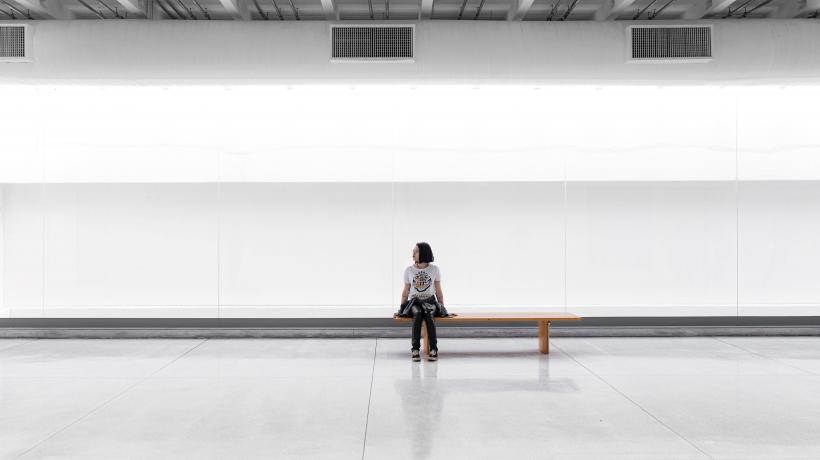 Frau sitzt auf einer Bank in einer großen, weißen Halle.