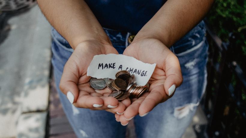 Hände, die Geld und einen Zettel mit der Aufschrift "Make a change" tragen