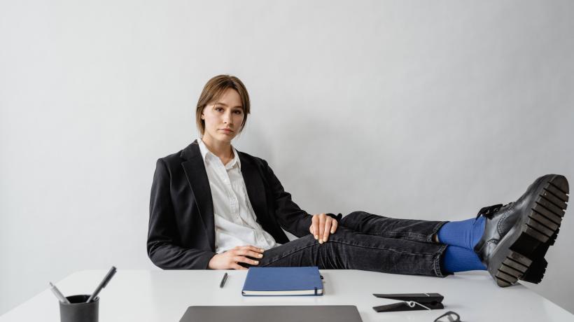 Eine junge Frau in lässiger Business-Kleidung sitzt am Schreibtisch und hat die Füße auf den Tisch gelegt.