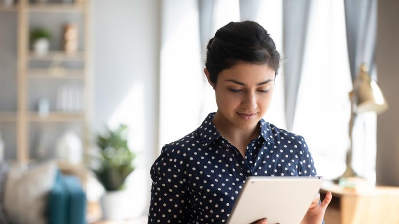 Foto: © fizkes – stock.adobe.com Eine junge Frau hält ein Tablet in der Hand und blickt darauf.