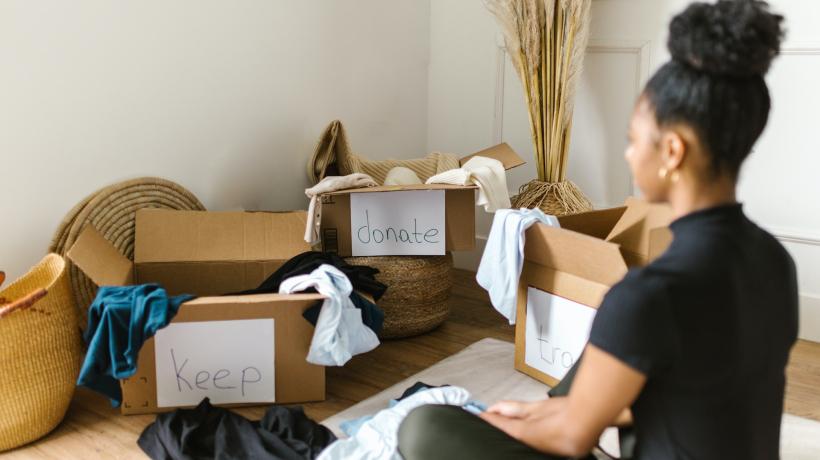 Eine Frau sitzt vor einigen Kartons und Taschen, aus denen Sachen heraushängen.