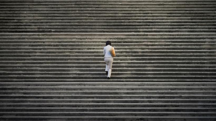 Eine Frau ist von hinten zu sehen, wie sie eine große und breite Treppe hinaufsteigt.