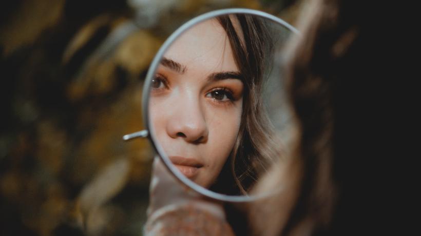 Eine junge Frau blickt ihr Gesicht im Spiegel an.