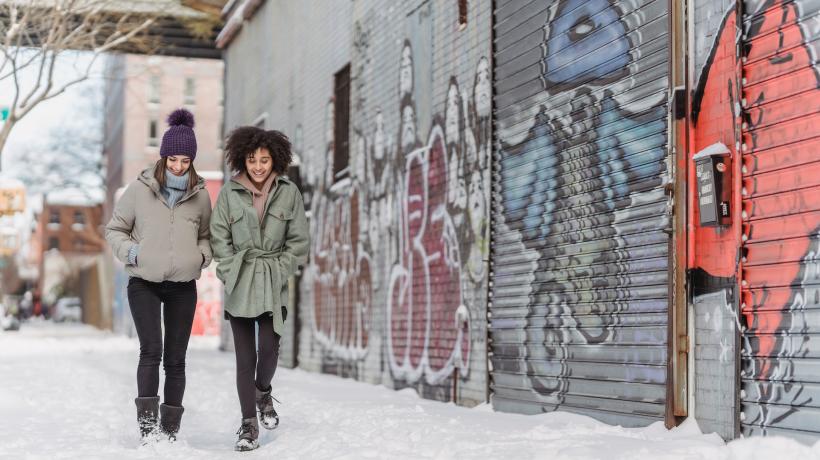 Zwei Frauen gehen dick eingepackt auf einem verschneiten Fußweg spazieren.