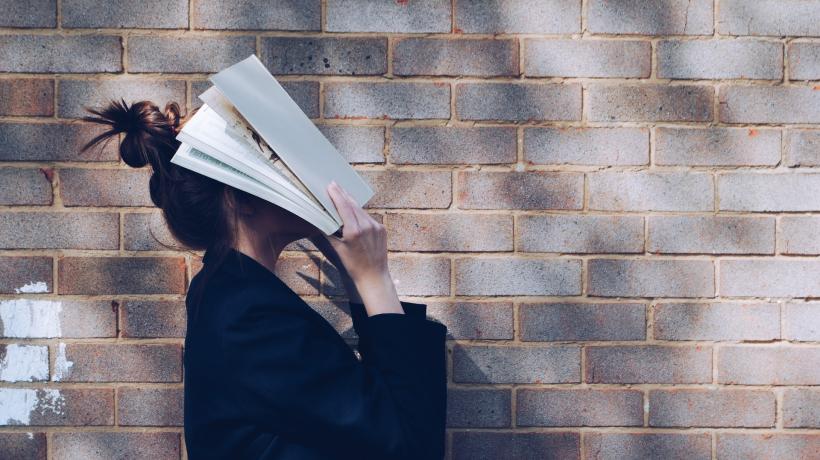 Eine Frau hält sich ein aufgeschlagenes Buch vors Gesicht.