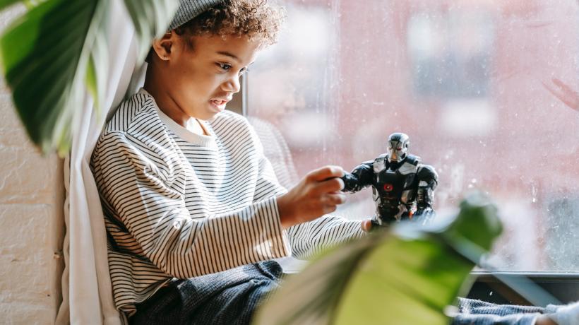 Ein Junge sitzt am Fenster und spielt mit einer Roboterfigur.