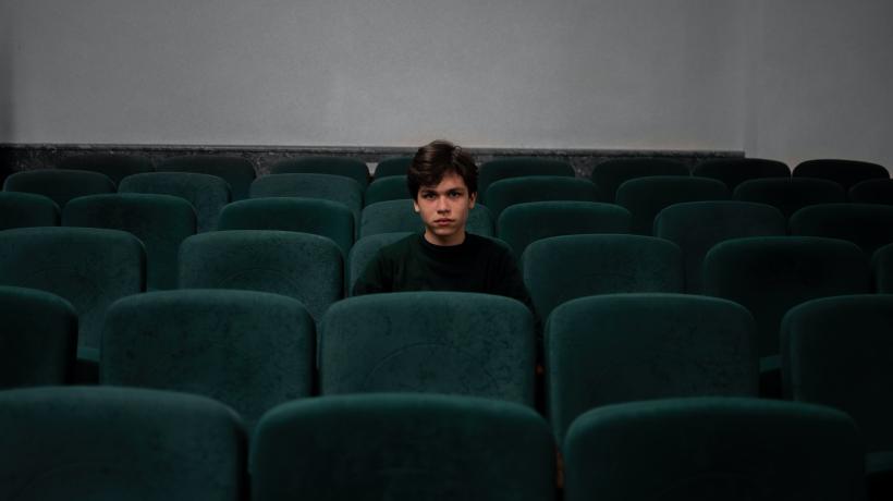 Ein junger Mann sitzt allein in einem Kinosaal.