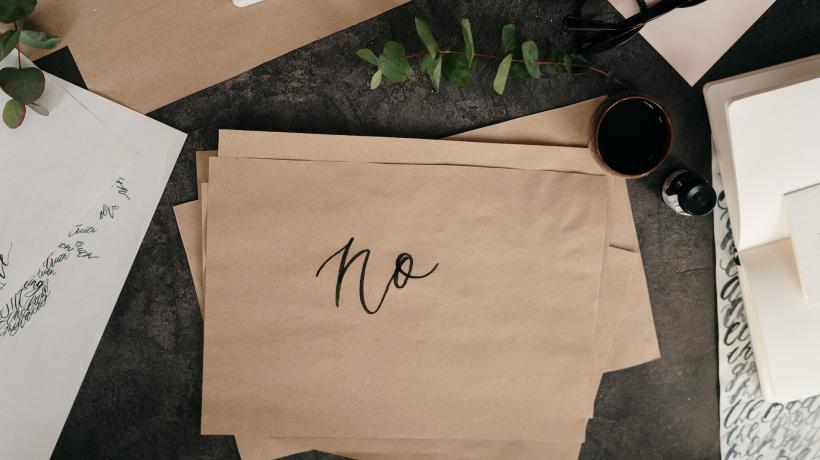 Auf einem Schreibtisch liegt ein Stapel mit hellbraunem Papier, auf das oberste Blatt ist "No" geschrieben.