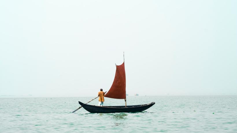 Eine Person steht auf offenem Wasser auf einem kleinen Segelboot.