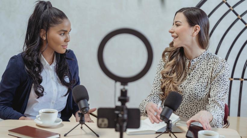 Zwei junge Frauen sitzen am Tisch vor zwei Mikrofonen und führen ein Interview.
