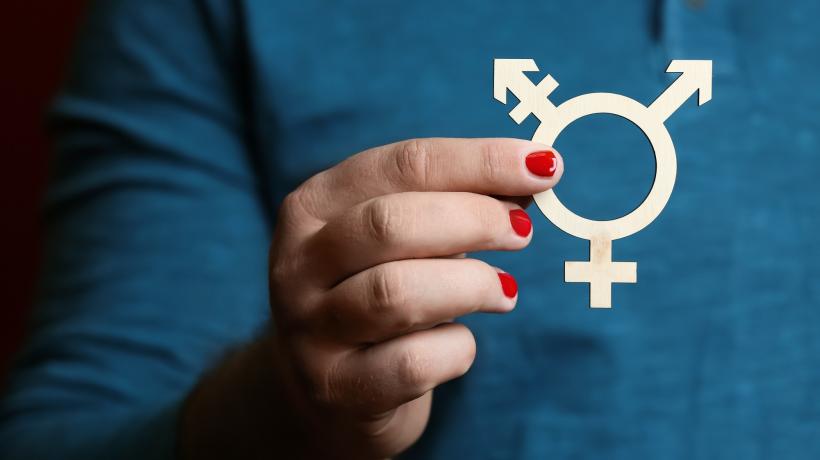 Foto: Pixel-Shot – stock.adobe.com Ein Mann mit rot lackierten Fingernägeln hält das Transgender-Symbol vor sich.