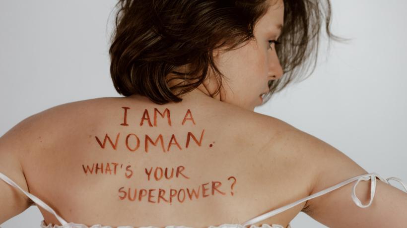 Auf dem Rücken einer Frau sind mit Stift die Sätze "I AM A WOMAN. WHAT'S YOUR SUPERPOWER?" geschrieben.