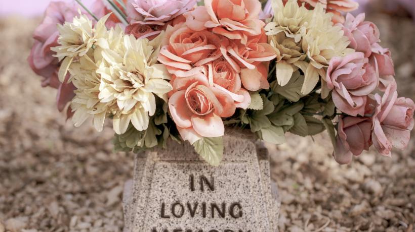 Blumen sind auf einem Grabstein abgelegt, auf dem "In Loving Memory" geschrieben steht.