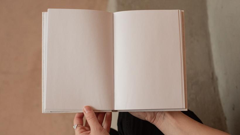 Eine Person hält ein aufgeschlagenes Buch in den Händen, dessen sichtbare Seiten leer sind.