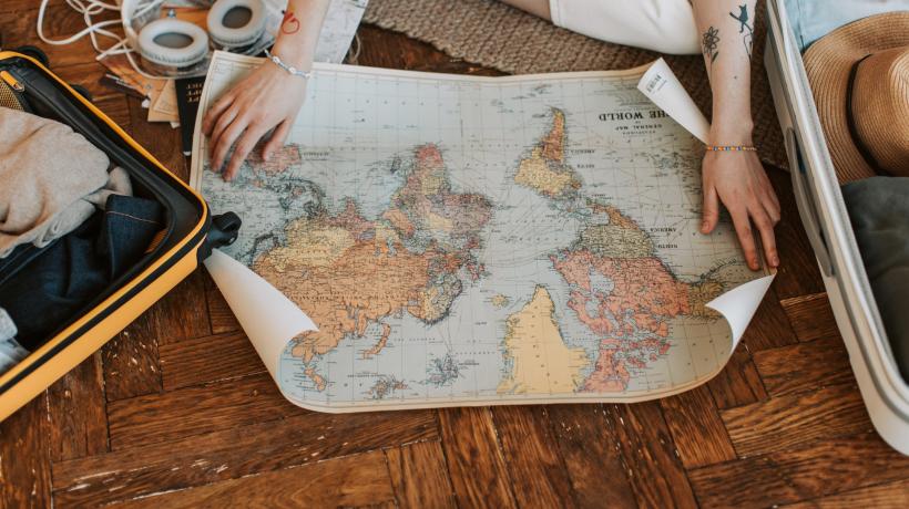 Eine Person sitzt auf dem Boden und breitet eine Weltkarte aus Papier aus.