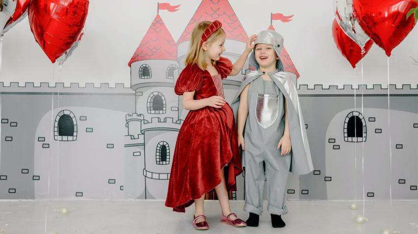 Ein Mädchen und ein Junge in mittelalterlich-höfischen Kostümen vor einer Burgkulisse