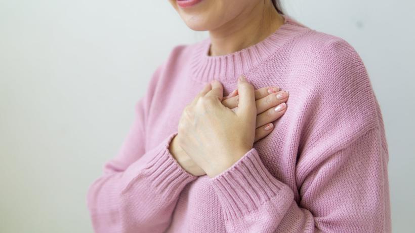 Eine Frau im rosa Pullover legt sich ihre Hände aufs Herz.