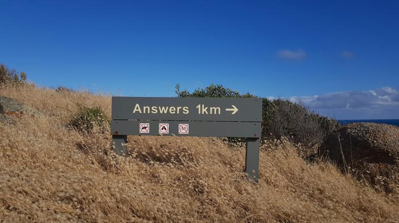 Ein Wegweiser in freier Natur, auf dem steht "Answers 1 km -->"