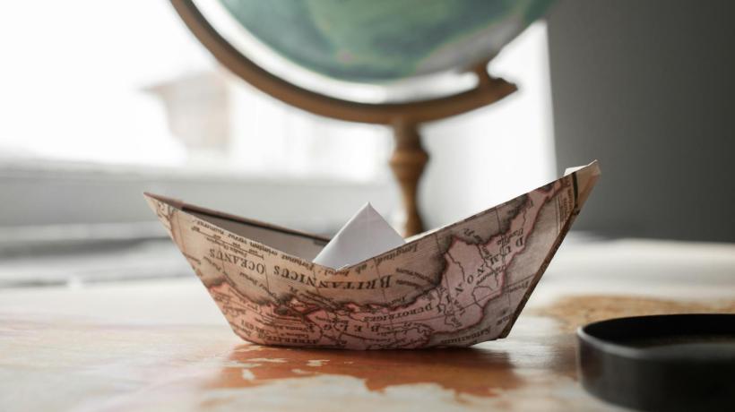 Ein gefaltetes Papierboot auf einem Tisch vor einem Globus