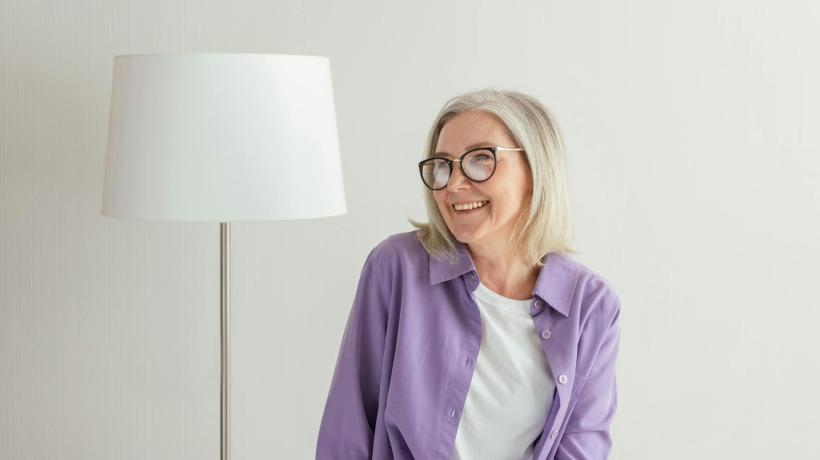 Eine ältere Frau steht lächelnd neben einer weißen Stehlampe.