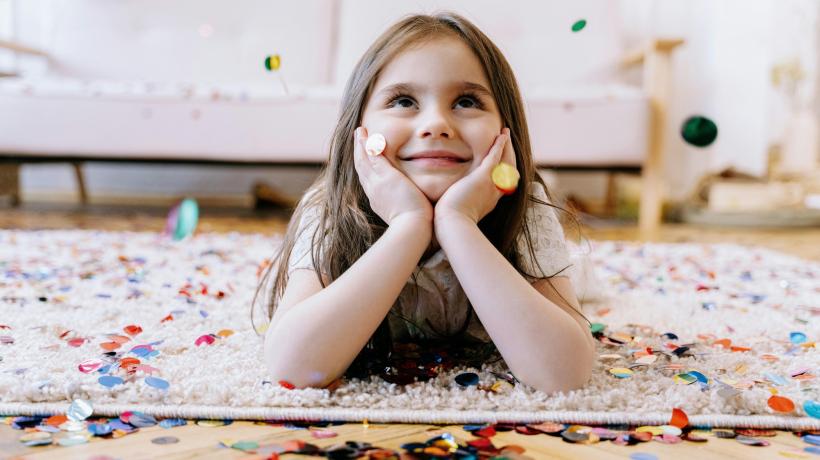 Foto: Ivan Samkov – pexels.com Ein junges Mädchen liegt bäuchlings auf dem Boden, um sie herum liegt Konfetti, sie lächelt.