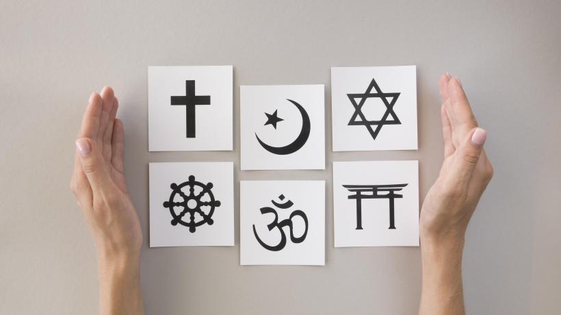 Zwei Hände umfassen sechs Kärtchen, auf denen die religiösen Symbole für das Christentum, den Islam, Judentum, Buddhismus, Hinduismus und Taoismus abgebildet sind