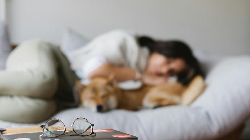 Eine Frau liegt zusammengekauert auf einem Sofa und hält ihren Hund im Arm