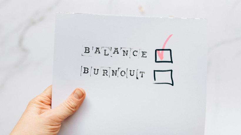 Eine Hand hält ein Papier, auf dem BALANCE und BURNOUT steht und BALANCE abgehakt wurde, BURNOUT nicht