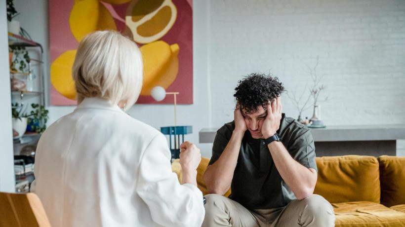 Foto: Timur Weber – pexels.com Ein Mann sitzt mit frustriert aufgestütztem Kopf vor einer Frau im Beratungszimmer.