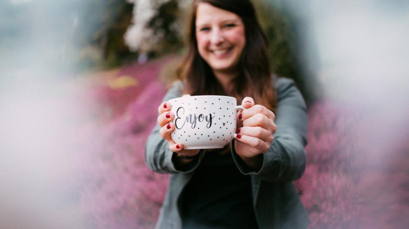 Autorin Barbara Klotz hält eine große Tasse mit der Aufschrift "Enjoy" in die Kamera.