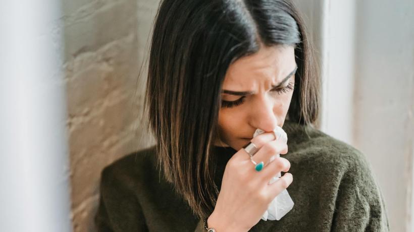 Foto: Liza Summer – pexels.com Eine dunkelhaarige Frau lehnt an einer Mauer und hält sich traurig ein Taschentuch vors Gesicht.