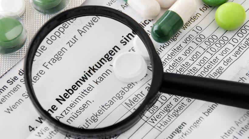 Foto: PhotoSG – stock.adobe.com Eine Lupe liegt auf einem Text und vergrößert das Wort "Nebenwirkungen"; drum herum liegen Pillen und Tabletten.